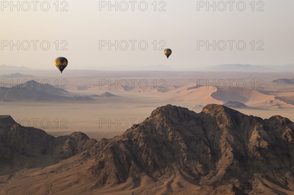 Two hot-air balloons above an arid plain and isolated mountain ridges at the edge of the Namib Desert. Aerial view from another balloon. Namibia