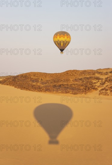 The hot-air balloon above an arid plain and isolated mountain ridges at the edge of the Namib Desert. The shadow is from a second balloon. Aerial view. Namibia