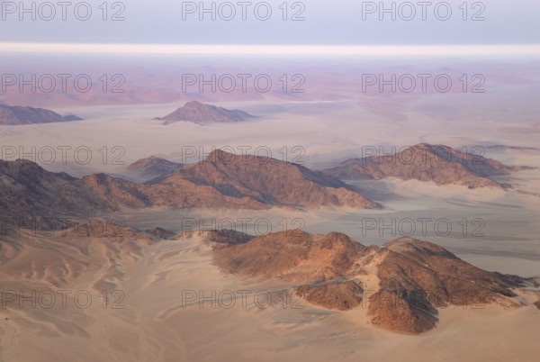 Arid plains and isolated mountain ridges at the edge of the Namib Desert. Early morning. Aerial view from a hot-air balloon. Kulala Wilderness Reserve, Namibia