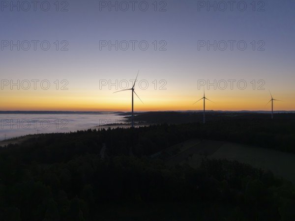 Three wind turbines in front of an orange and blue sky at sunrise with fog, near Schorndorf, Remstal, Rems-Murr-Kreis, Baden-Württemberg, Germany