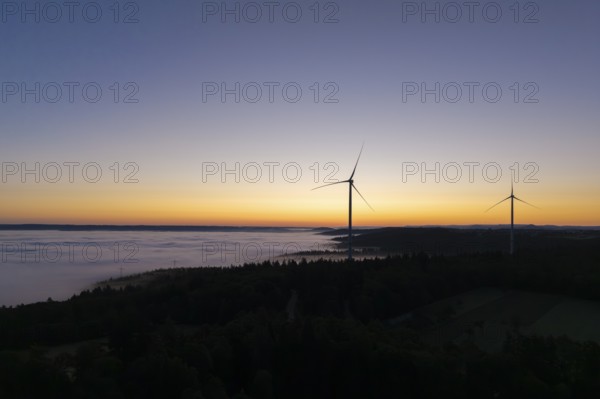 Two wind turbines in front of a colourful sunrise sky with fog over the landscape, near Schorndorf, Remstal, Rems-Murr-Kreis, Baden-Württemberg, Germany