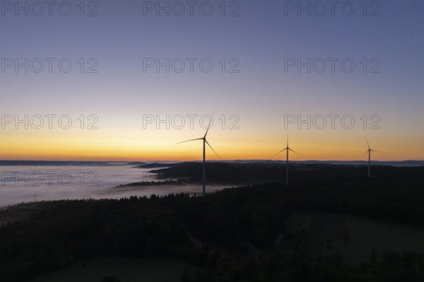 Wind turbines in front of a bright blue and orange sky at sunrise with fog over the landscape, near Schorndorf, Rems-Murr district, Rems-Murr-Kreis, Baden-Württemberg, Germany