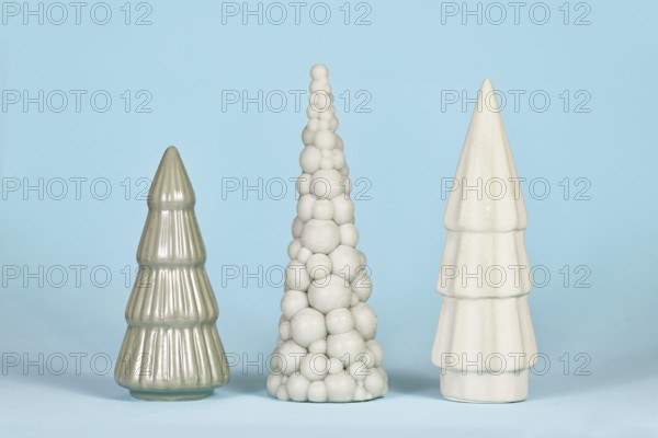 Three different shaped light green ceramic Christmas trees on blue background