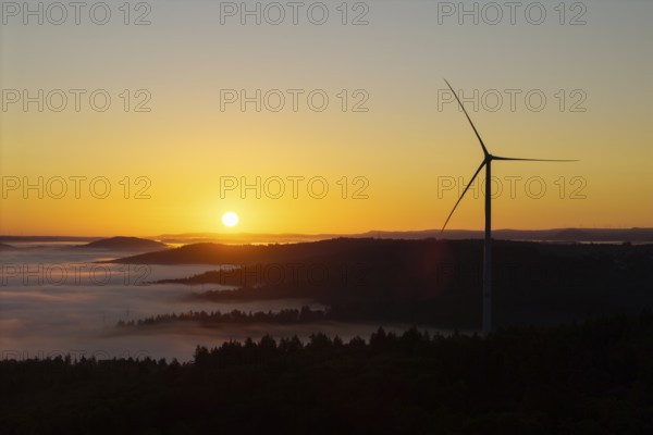 A wind turbine stands over the hills in front of sunrise, near Schorndorf, Rems-Murr district, Rems-Murr-Kreis, Baden-Württemberg, Germany