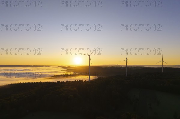 Three wind turbines overlook a fog-covered forest at sunrise, near Schorndorf, Rems-Murr district, Rems-Murr-Kreis, Baden-Württemberg, Germany