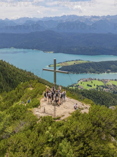 Group around a cross on a mountain peak with a panoramic view of the surrounding lakes, Herzogstand summit, Walchensee, Schlehdorf, Germany