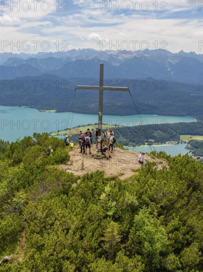 People standing around a summit cross with a view of the surrounding landscape, Herzogstand summit, Walchensee, Schlehdorf, Germany