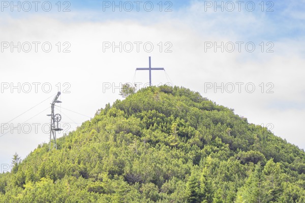 A cross is enthroned on a green mountain peak under a slightly cloudy sky, Herzogstand summit, Walchensee, Schlehdorf, Germany