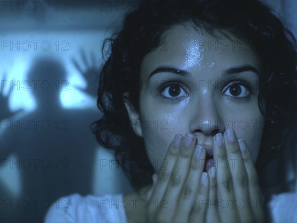A woman gripped by fear, behind her an eerie silhouette of a shadow, symbolic image for anxiety disorders, panic attacks, mental illness, AI generated, AI generated