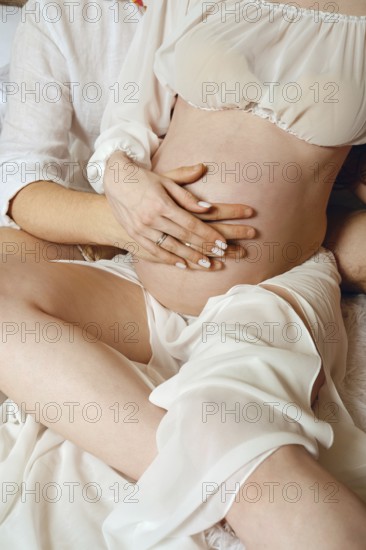 A man and woman share a tender moment as they prepare to welcome their first child. They are seated comfortably, with his hands resting gently on her baby bump, radiating love and connection