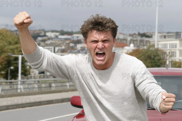 A man shouts angrily with clenched fists on a road, symbolic image for aggressive behaviour in road traffic, AI generated