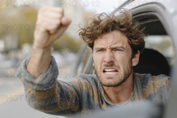 A man in a car shows a clenched fist and looks angrily out of the window on a street, symbolic image for aggressive behaviour in road traffic, AI generated
