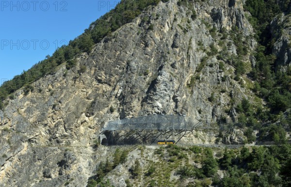 Yellow Swiss Post bus travelling under the safety nets against falling rocks to the Petits Pontis tunnel, cantonal road in Val d'Anniviers, Valais, Switzerland