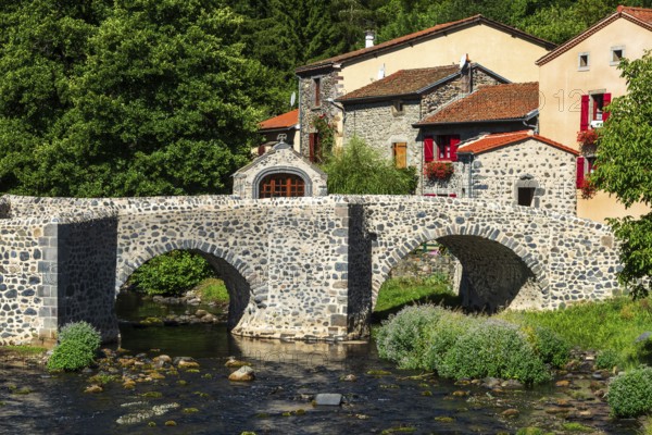 Stone bridge over the Pavin couze river flowing through the village of Saurier, Puy de Dome. Auvergne Rhone Alpes, France