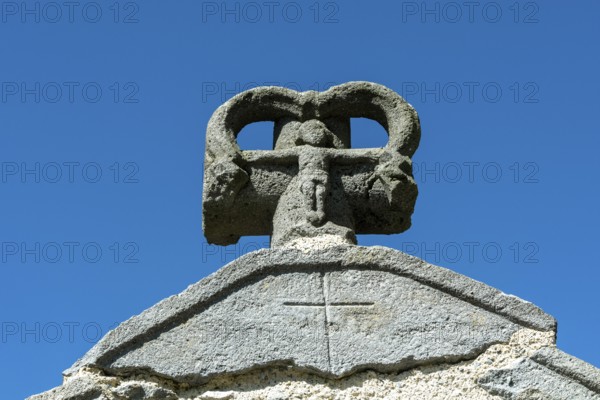 Stone cross on the bridge over the Pavin couze river flowing through the village of Saurier, Puy de Dome. Auvergne Rhone Alpes, France