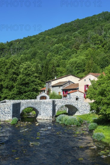 Stone bridge over the Pavin couze river flowing through the village of Saurier, Puy de Dome. Auvergne Rhone Alpes, France