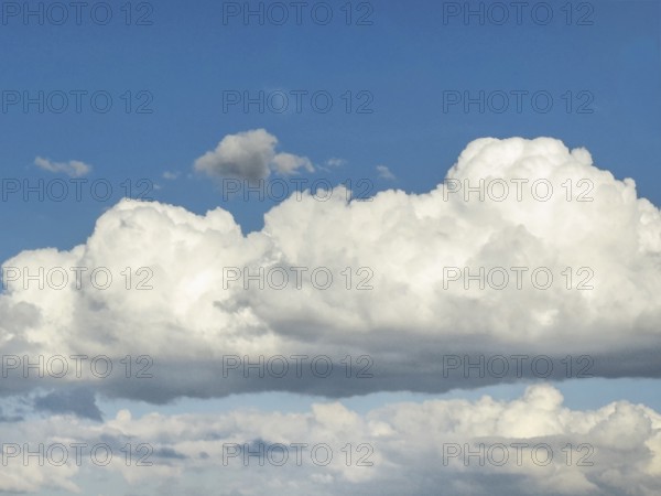 In the centre of the picture large stratocumulus cluster cloud in front of a sky-blue sky, below in the background many cumulus cluster clouds, international