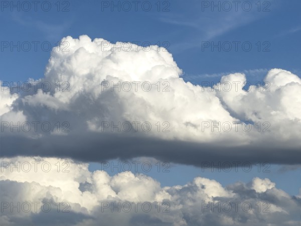 Stratocumulus in the centre of the picture, dense cloud cover from many cumulus clouds in the background, bright blue sky above, international