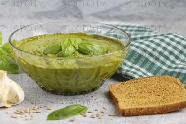 Basil pesto in a glass bowl with bread, garlic and chequered cloth