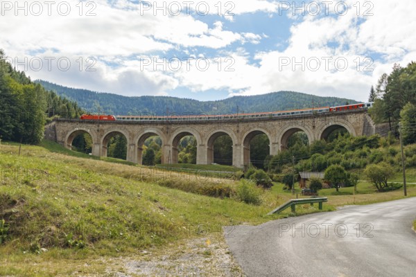 Train crossing Adlitzgraben viaduct, cloudy sky and green hills, Semmering railway, Semmering, Lower Austria, Austria
