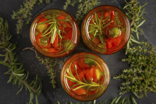Top view of three jars of herbs and chilli peppers surrounded by rosemary and thyme