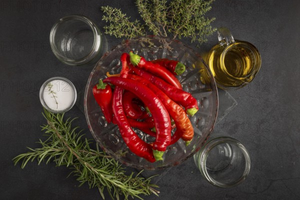 Several red peppers, chilli peppers alongside oil, salt, herbs and empty jars