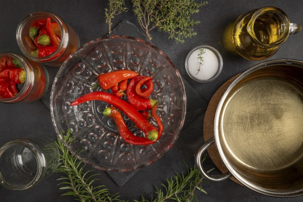 Hot peppers in jars and bowl, next to it an open cooking pot on a dark background