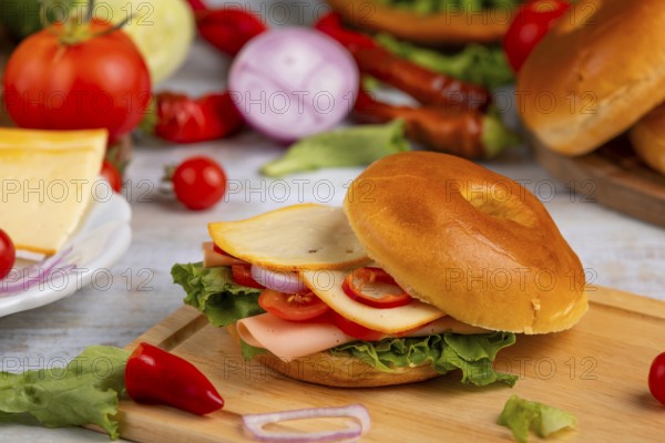 A bagel topped with cheese, sausage, tomatoes, onion and lettuce leaves on a wooden board