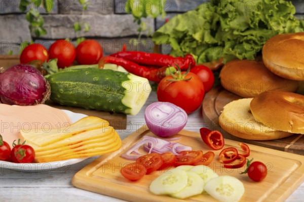 Bagels alongside sausage, cheese and fresh vegetables such as tomatoes, lettuce, cucumber and peppers