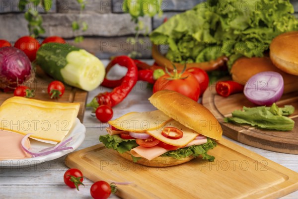A bagel topped with cheese, sausage, salad and vegetables, surrounded by fresh ingredients