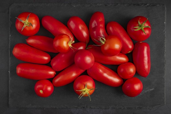 Different types of tomatoes lie on a dark slate slab