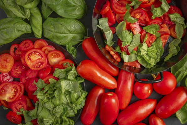 Pan and plate with sliced tomatoes and basil leaves, surrounded by fresh vegetables