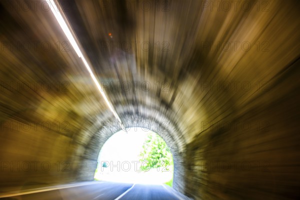 View from car during fast driving by car driver speeding car racer through long tunnel with straight tunnel tube and light at the end of long long tunnel of a long tunnel above narrow light strips ceiling lighting, international