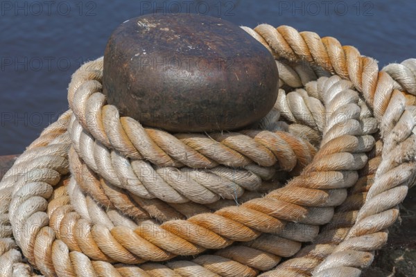 Ropes knotted around a metal bollard, beige and brown, rich in contrast against a dark blue background, East Frisia, Lower Saxony, Germany