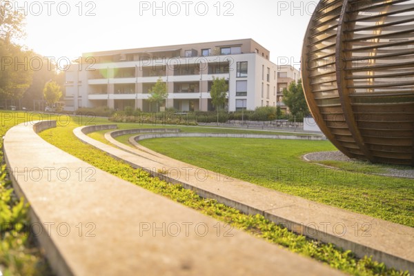 Wooden sphere-shaped structure next to modern residential complex in sun-drenched park, small town of Perle Nagold, Black Forest, Germany