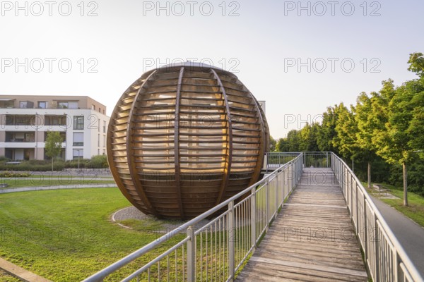 Wooden spherical structure in front of modern residential building at sunset in urban park, small town of Perle Nagold, Black Forest, Germany