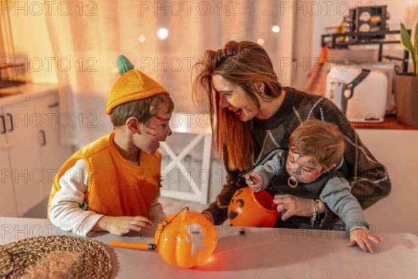 Mother and children wearing halloween costumes are sitting at a table in their kitchen, playing with pumpkin baskets full of candies