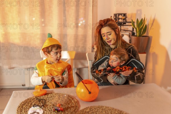 Mother and children wearing halloween costumes and painted faces, celebrating at home with candies and pumpkin decorations