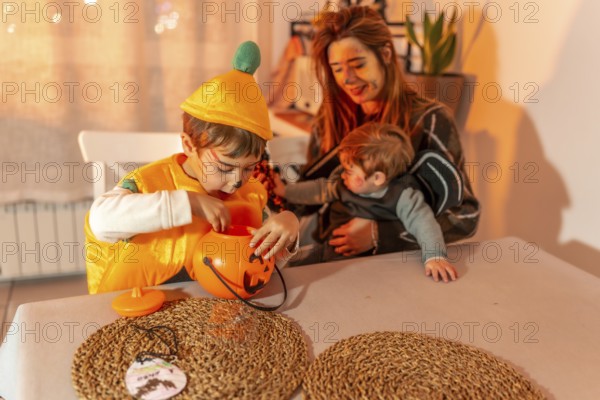 Two young brothers wearing halloween costumes are playing at a table with their mother, enjoying the festive atmosphere