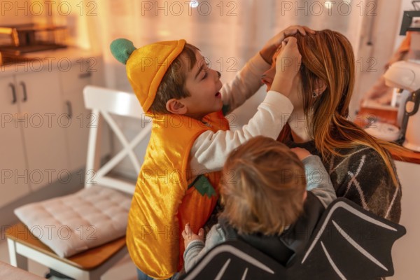 Two brothers, dressed up in halloween costumes, applying makeup on their mother's face, creating a playful and festive atmosphere in their home