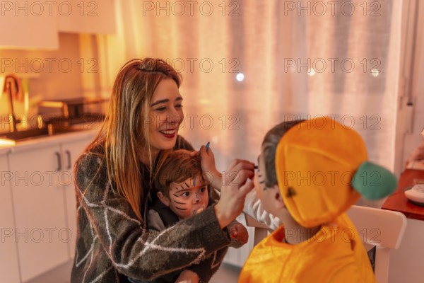 Happy family preparing for halloween party, mother applying makeup on children's faces, creating festive atmosphere