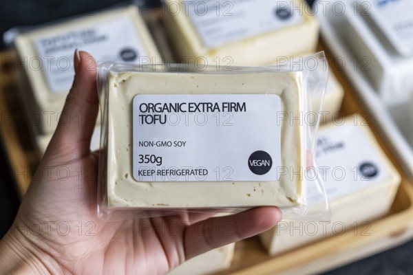 Hand holding firm tofu block in front of supermarket refrigerator. Concept of plant-based protein and vegan grocery shopping. Generative AI, AI generated