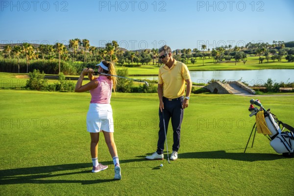 Golfer practicing her swing with coach on beautiful golf course, working on improving her technique