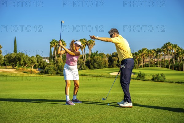 Experienced golf instructor guiding a female golfer on a sunny day, providing tips for a perfect swing on a lush green course