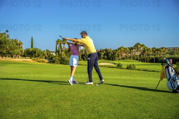 Middle aged golf instructor assisting young woman golfer on improving her swing on a sunny day at the golf course