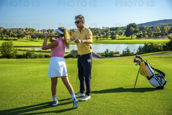 Golf instructor guiding a womans swing on a sunny golf course, showcasing technique and precision under a bright blue sky