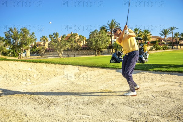 Professional golfer hitting a ball out of a sand trap on a sunny day, showcasing skill and precision on the lush green golf course
