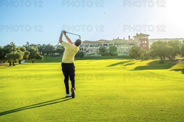 Golfer swings his club on a beautiful, sunny day, aiming for the green with a luxurious resort in the background