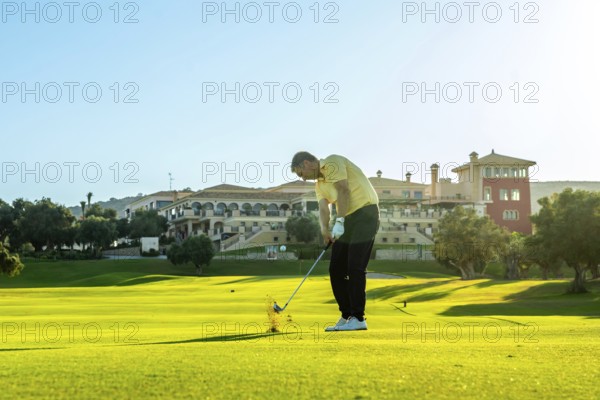 Golfer takes a swing, sending the ball flying across a vibrant green golf course, with a luxurious clubhouse in the background