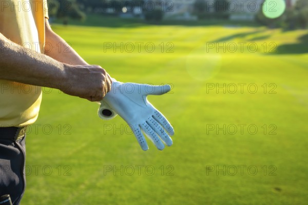 Golfer putting on a white golf glove, getting ready for an exciting game on a lush, vibrant green golf course under the summer sun